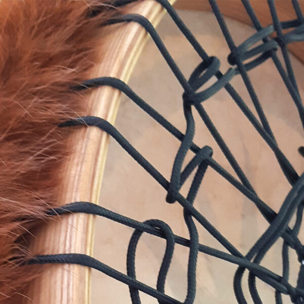 Abbildung: Detailaufnahme des naturfarbigen Eschenholz-Rahmens mit schwarzer Schnurbespannung und überstehendem Fellrand